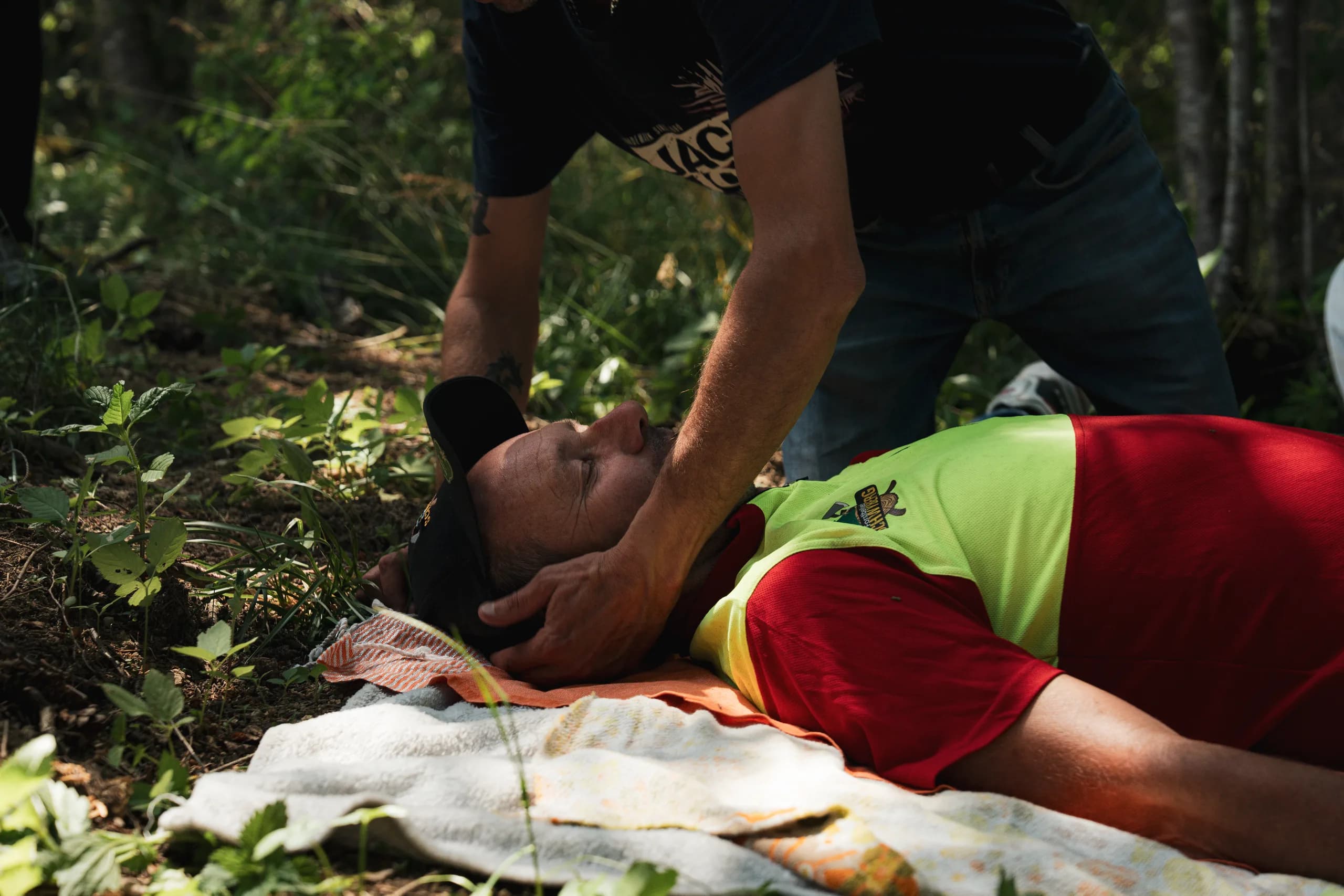 En forêt, un participant tient la tête d'un homme allongé sur le dos et lui soulève le menton